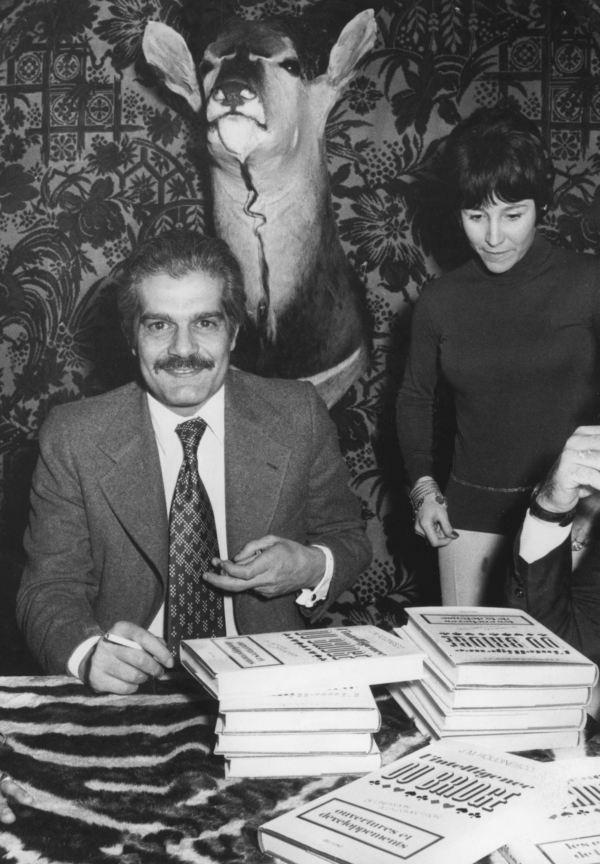 Egyptian actor and championship bridge player Omar Sharif, who was delayed en route to a bridge tournament, signing copies of 'L'intelligence du Bridge,' by J.M. Roudinesco, in a Parisian club decorated in a safari motif on 22nd February 1973.(FILM) AFP PHOTO (Photo by AFP) 