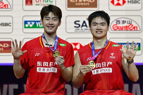 China's Liang Wei Keng (R) and Wang Chang celebrate on the podium during an awards ceremony after winning against Malaysia's Aaron Chia and Soh Wooi Yik in their BWF World Championships men's doubles final badminton match at the Indira Gandhi Indoor Stadium in New Delhi on August 23, 2026.