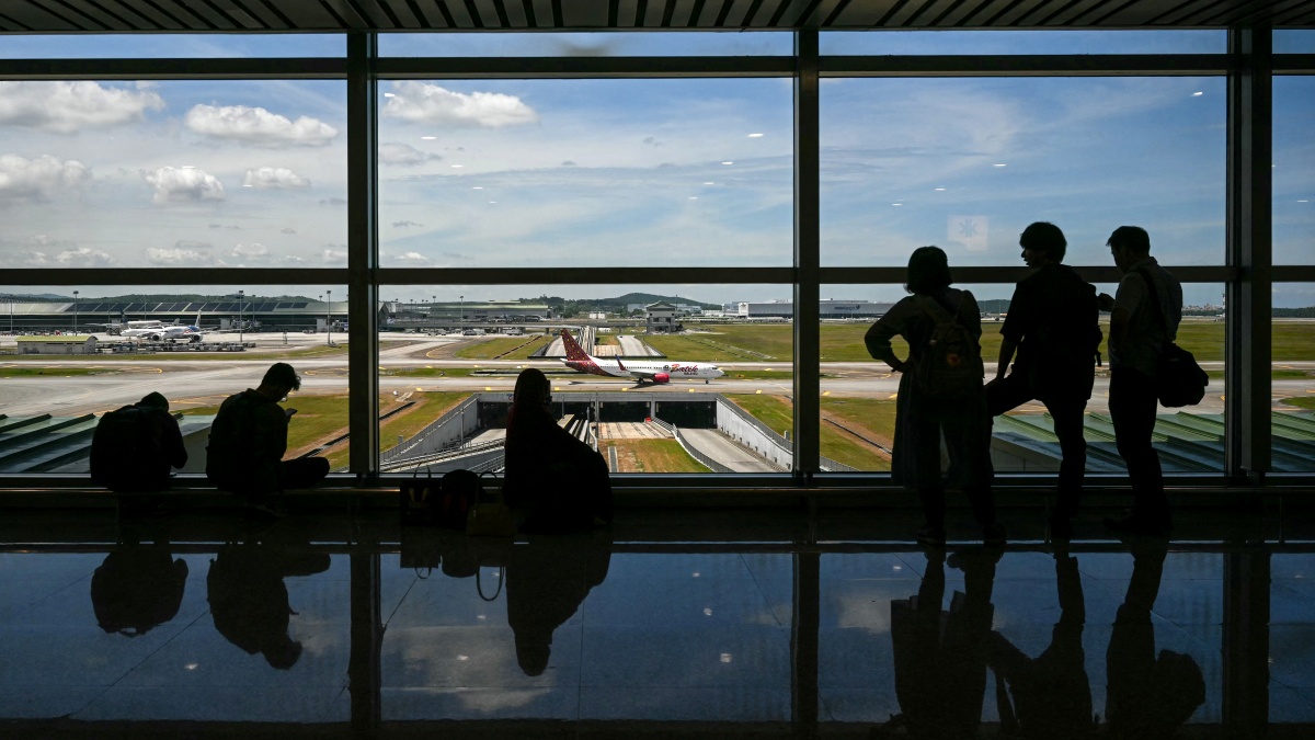 2025年8月12日,旅客在吉隆坡國際機場觀看一架飛機在跑道上滑行。(Mohd RASFAN / AFP via Getty Images)